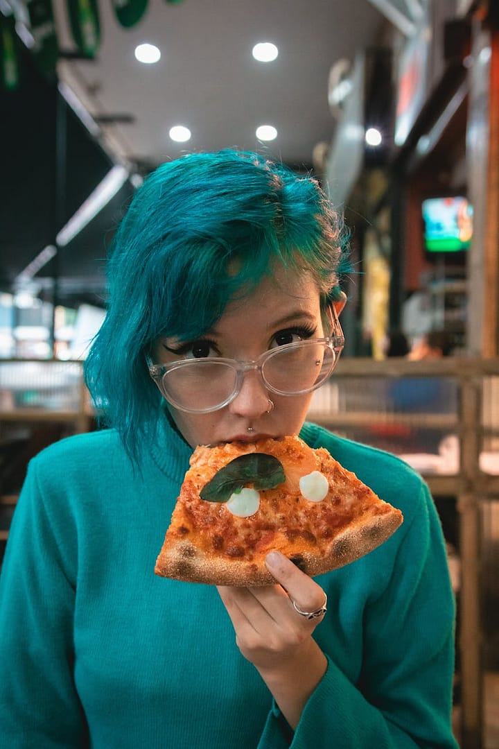 green haired woman eating pizza